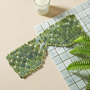 Green woven mat on a tiled surface with a candle and leaf decoration.