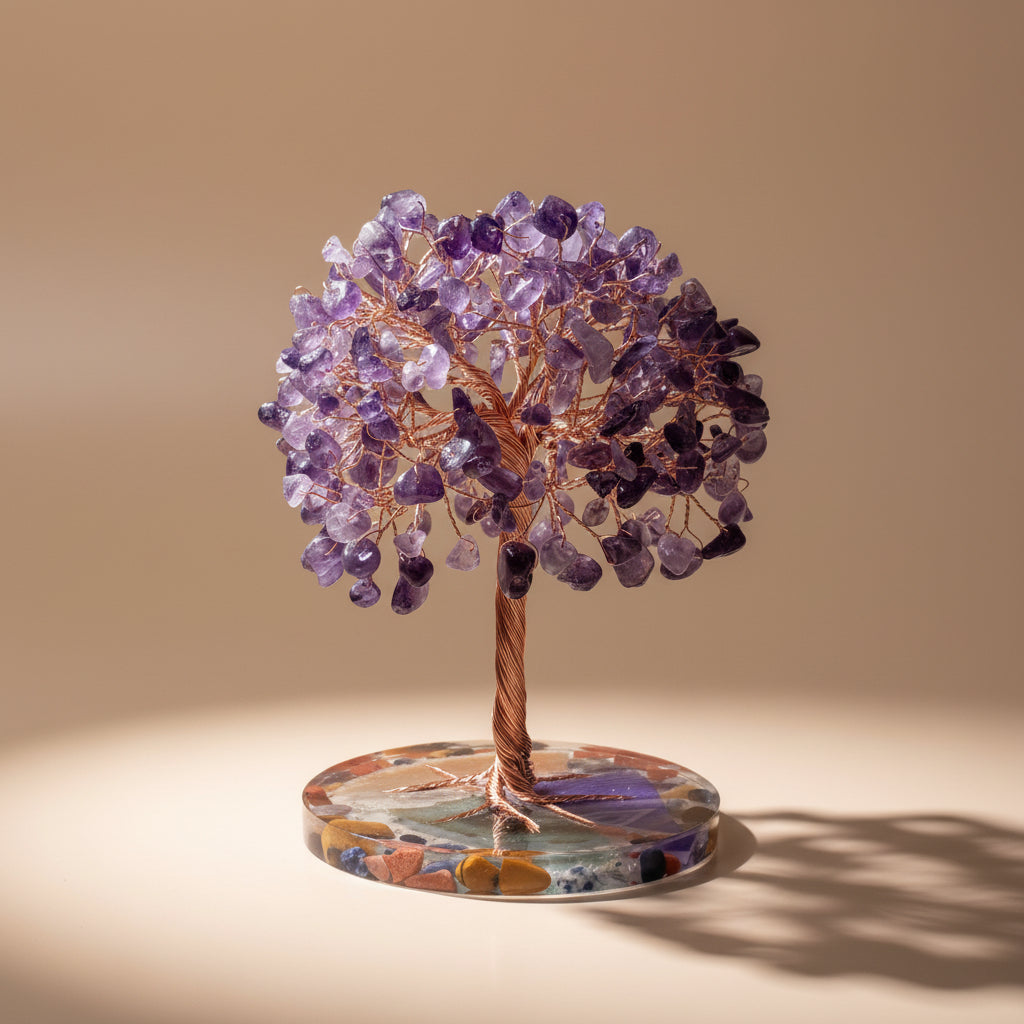 Crystal tree with purple stones on a colorful base, placed on a surface with a book and decorative object in the background.