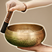 Person holding a bronze singing bowl with a wooden mallet, with water splashing inside.